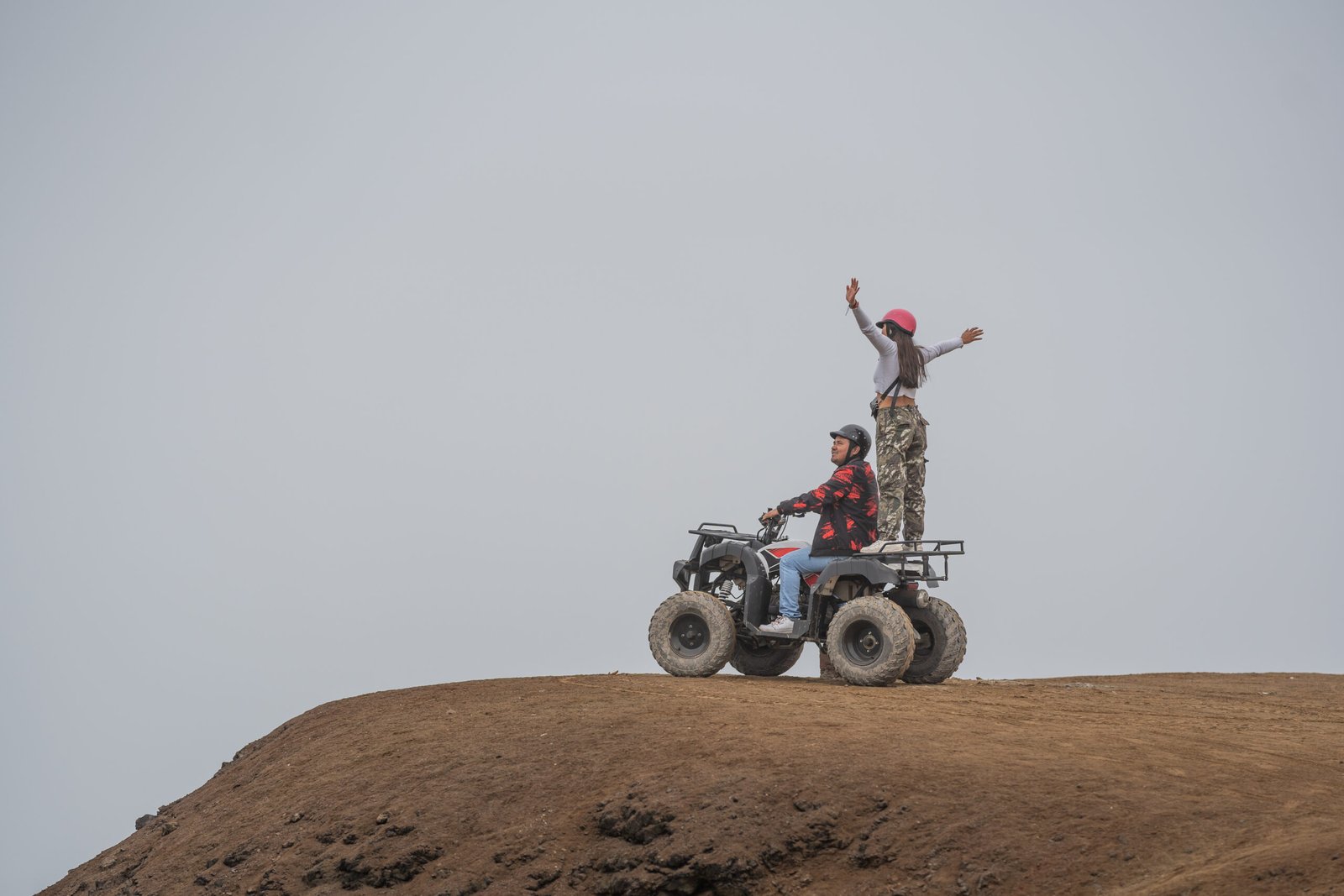 Two friends on a quad bike on the edge of a hill gesturing freedom