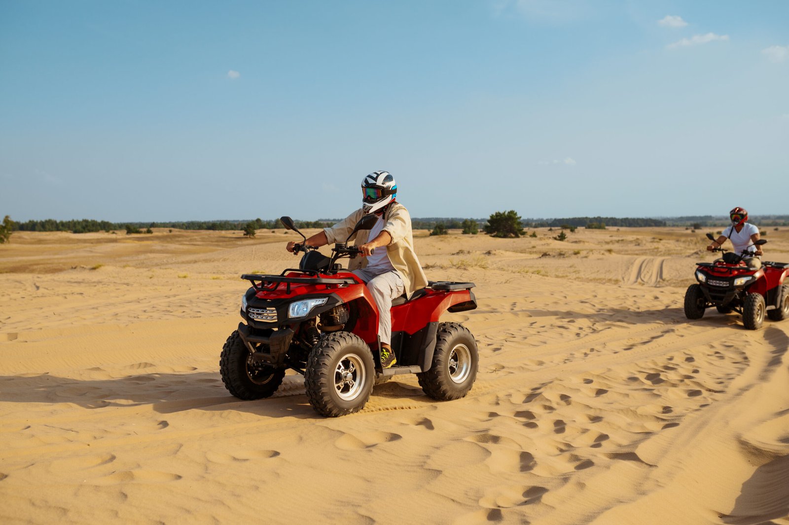 Two men in helmets and glasses ride on atv in desert. Male persons on quad bikes, sandy race, dune safari in hot sunny day, 4x4 extreme adventure, quad-biking
